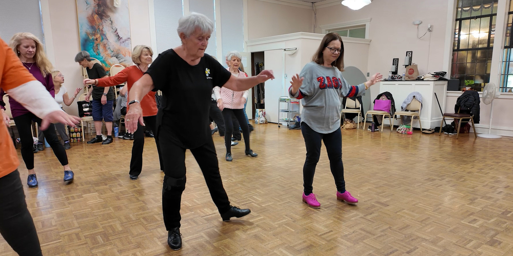 Older women practice tap dancing in a studio.