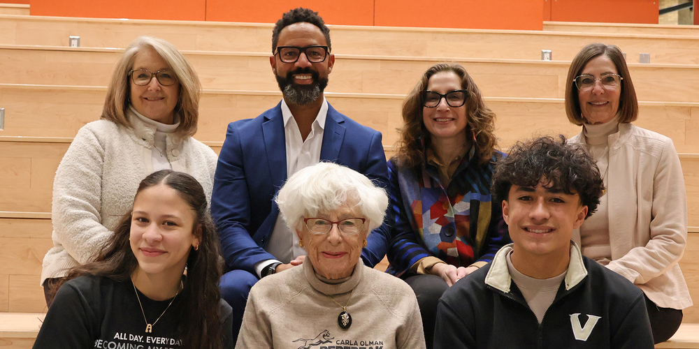 Two students smile while seated with Carla Peperzak and other adults.