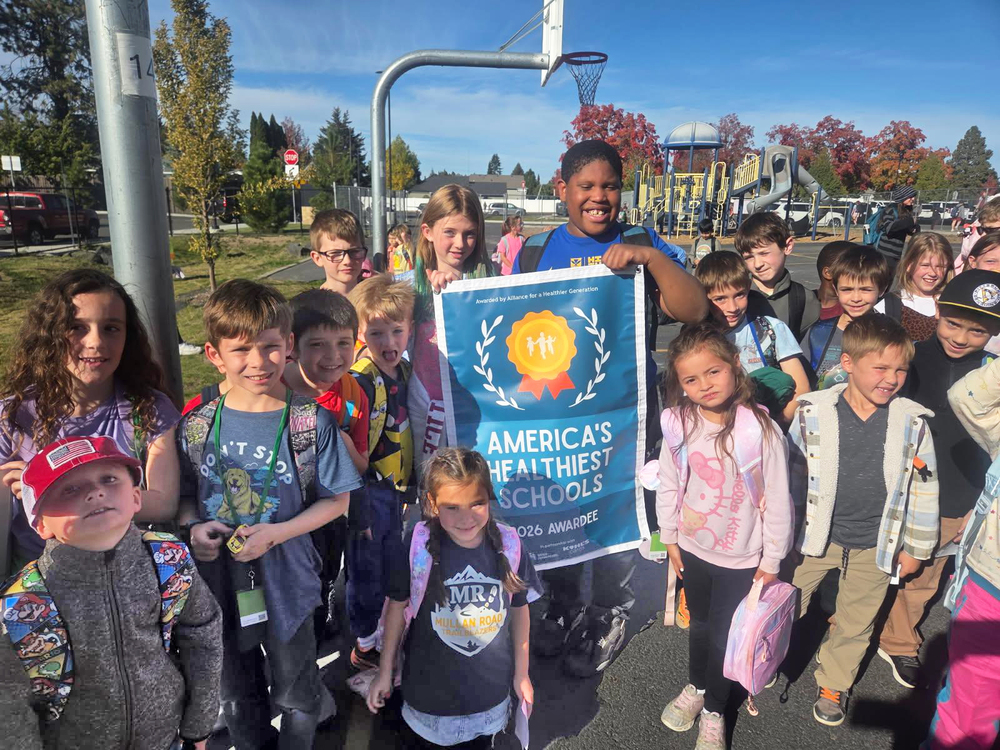 Mullan Road Elementary School students smile on a playground with a banner for America's Healthiest Schools.