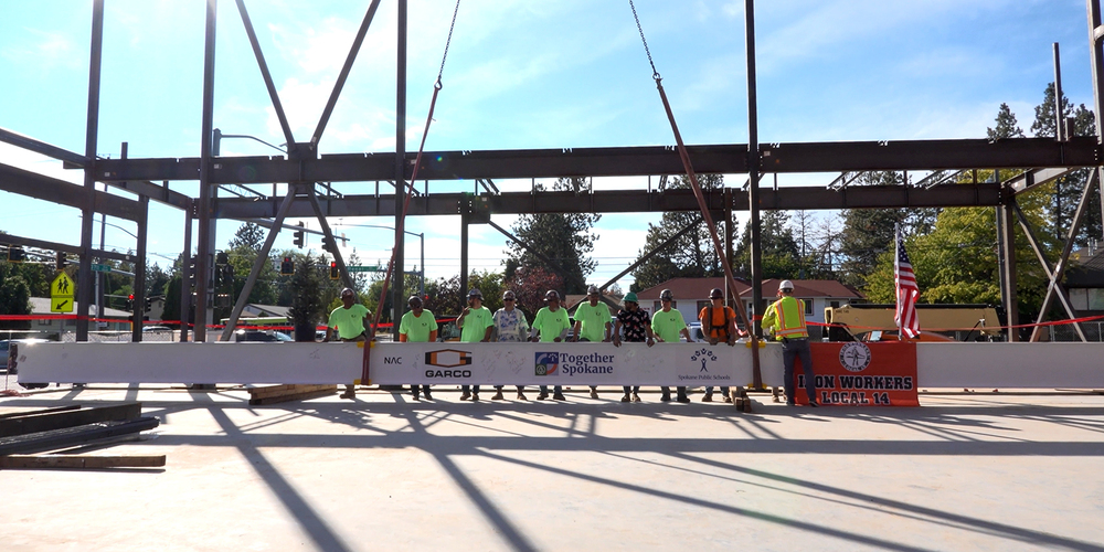 Construction crew members stand with a signed steel beam before it is lifted into place.