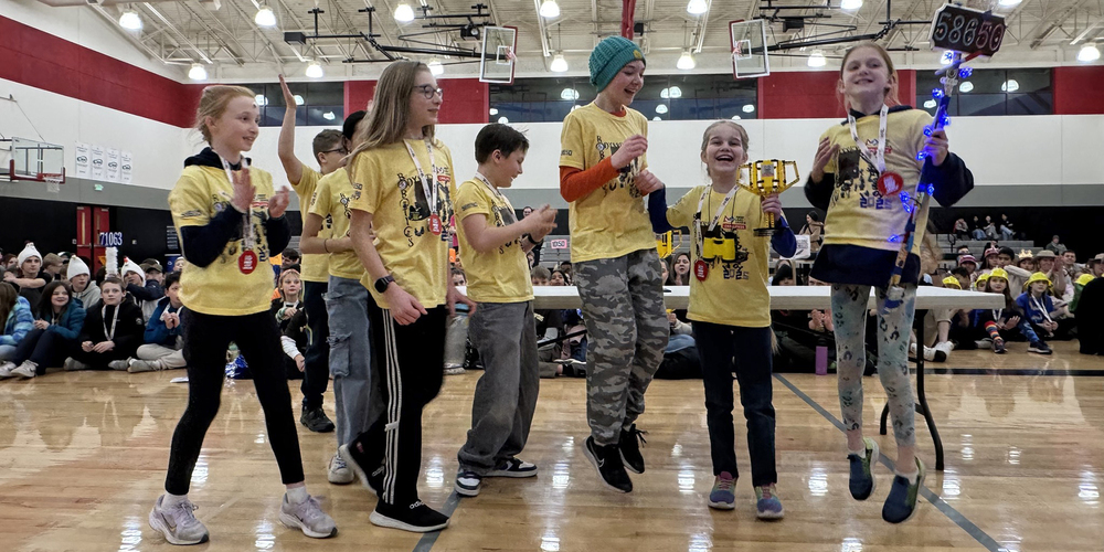  Odyssey at Libby students wearing yellow shirts smile and jump enthusiastically as they receive a LEGO trophy. 