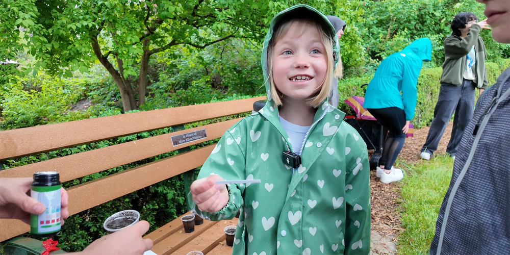 An elementary student in a park smiles as she tests soil on a field trip in a park.