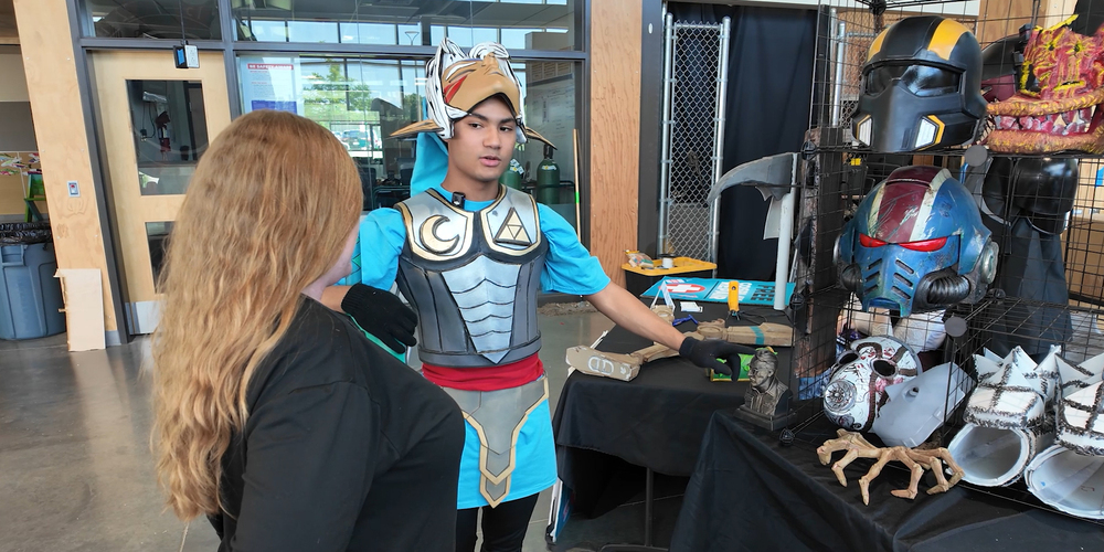 An On Track Academy student displays fantasy costumes and props they made on a table at a showcase event.