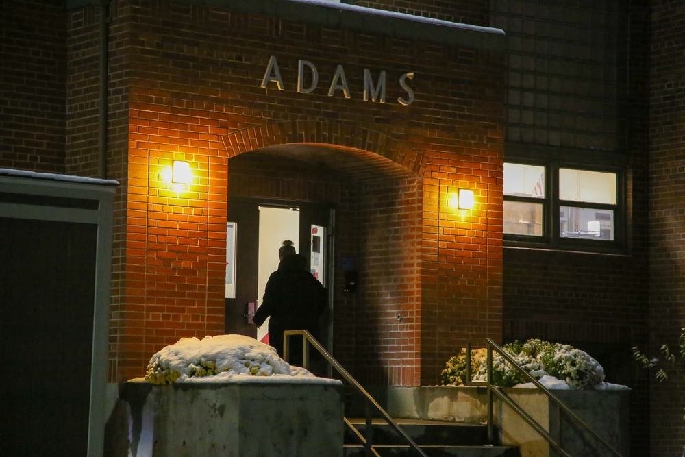 Woman walks into Adams Elementary front entrance at night.