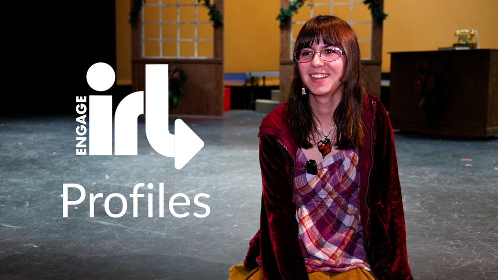 A high school student smiles while seated on a stage with the sets for a play behind her. The text reads Engage IRL profiles.