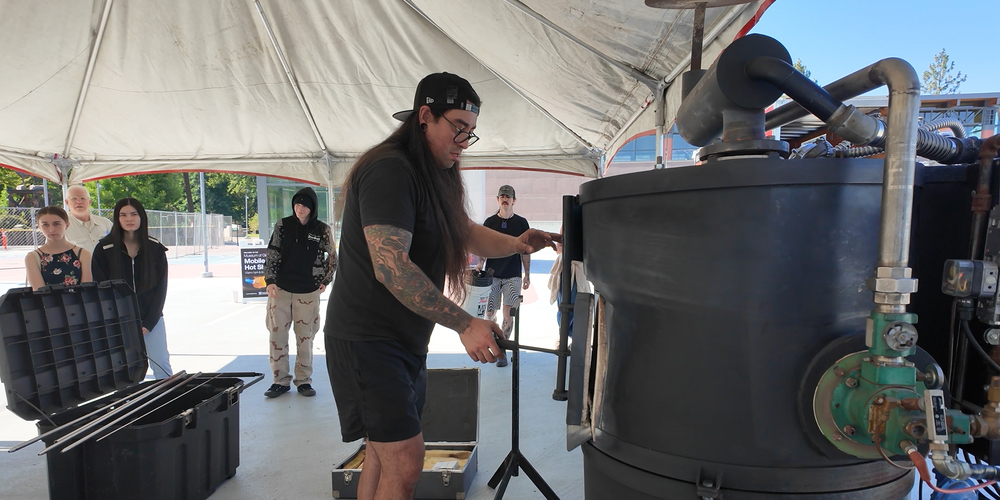 A glass artist sets up an outdoor studio while students watch.