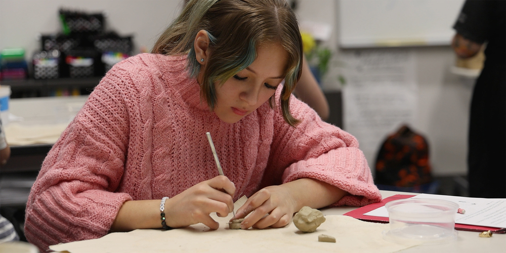 A middle school student uses a needle to score clay in art class.