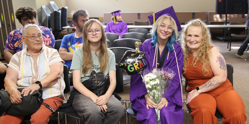 A Rogers High School graduate smiles with family while holding flowers and balloons.