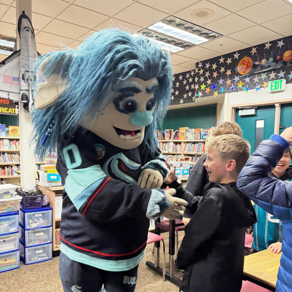 Bouy, the Seattle Kraken sea-troll mascot, greets elementary students in the school library.