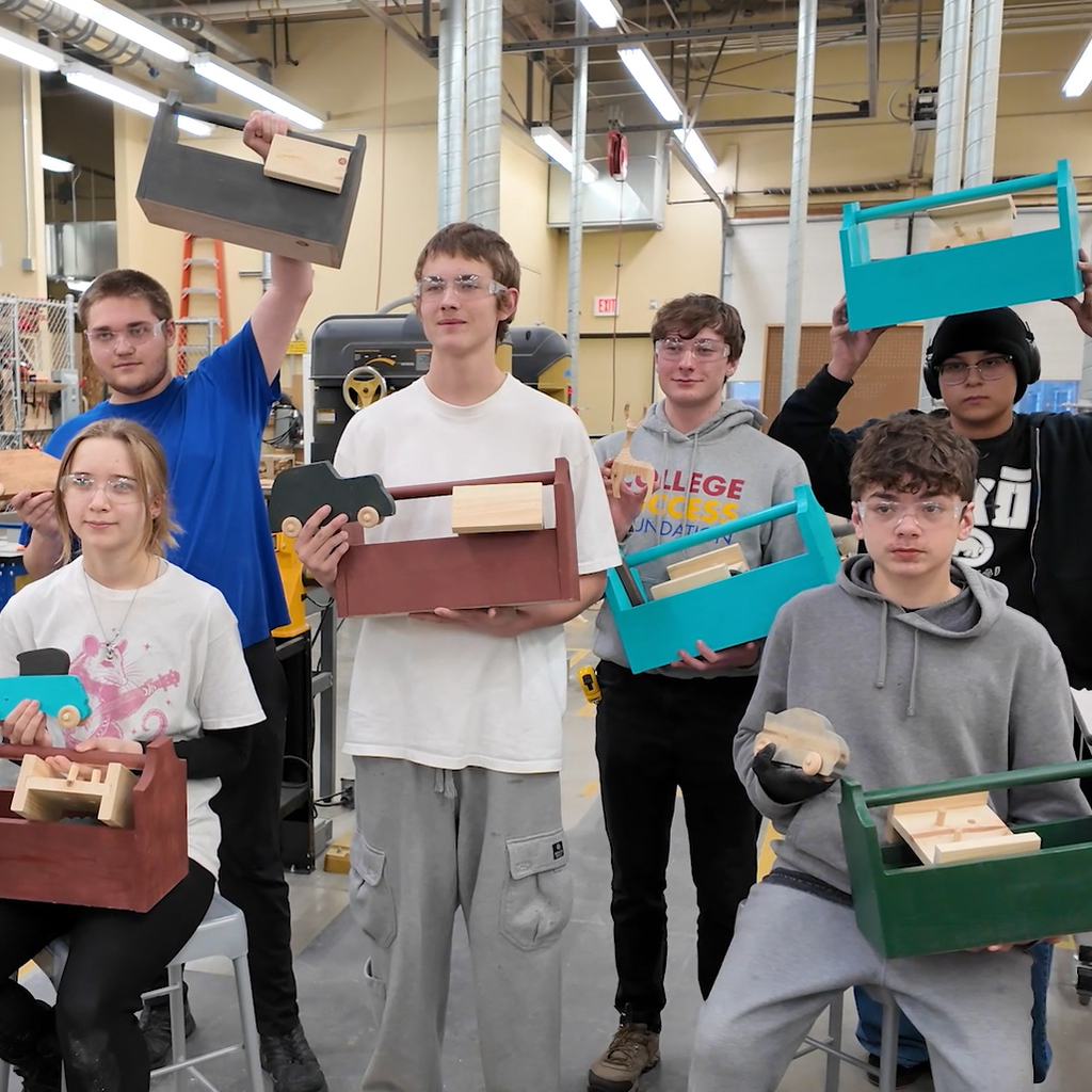 Six Rogers high school students hold wooden toolboxes and toys they made to distribute to a holiday assistance program.