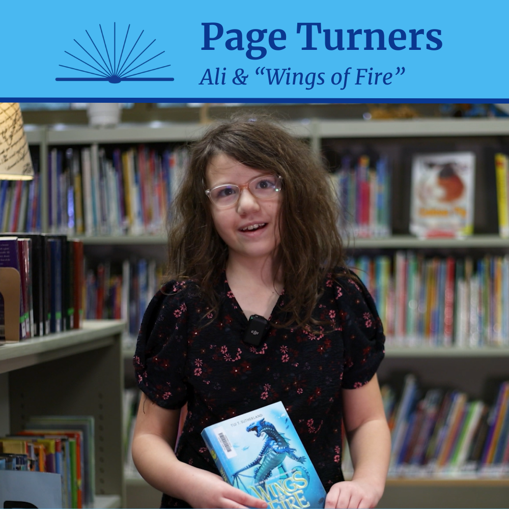 A Holmes Elementary School student holds a book with a dragon on the cover in a school library. Accompanying text is Page Turners: "Ali & Wings of Fire"