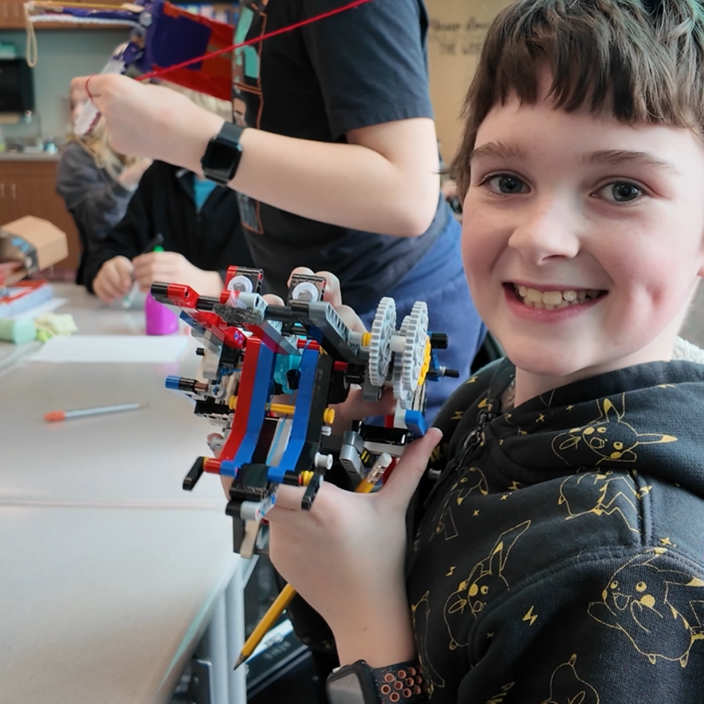 An Odyssey student smiles while displaying a prosethic arm they designed with K'NEX gears.