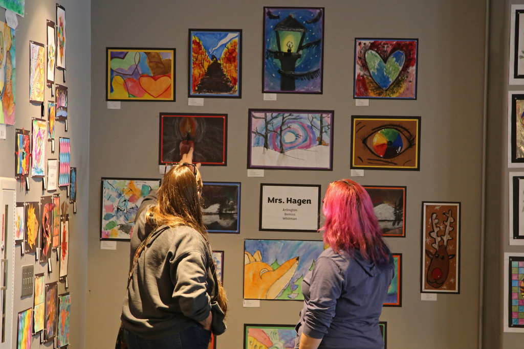 Two teachers look at student artwork displayed in a gallery.