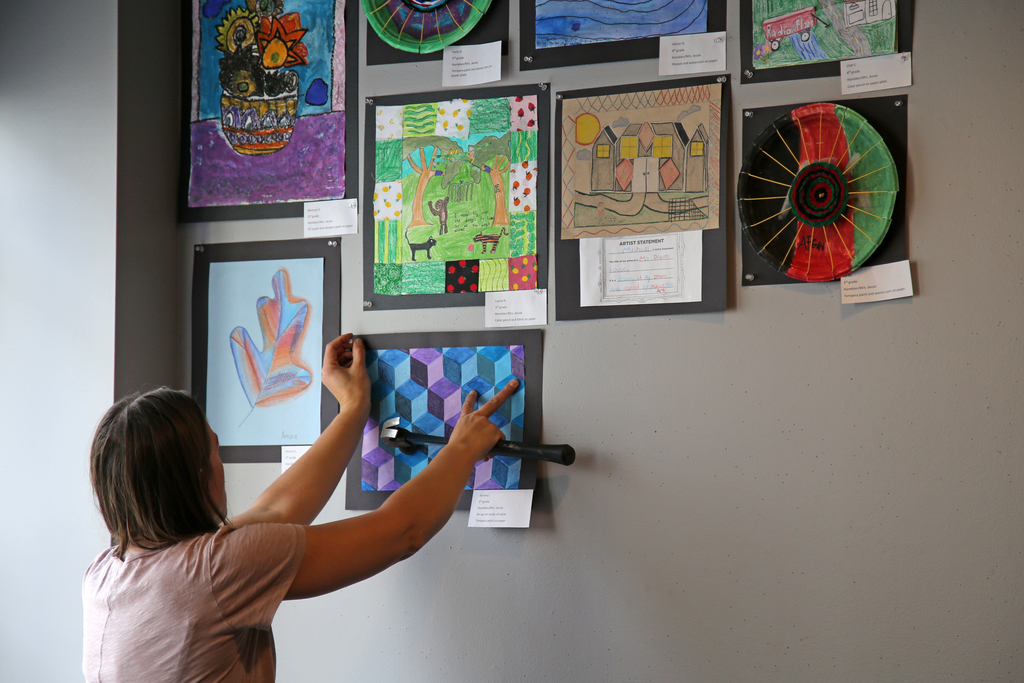 A teacher hangs student artwork in a gallery.