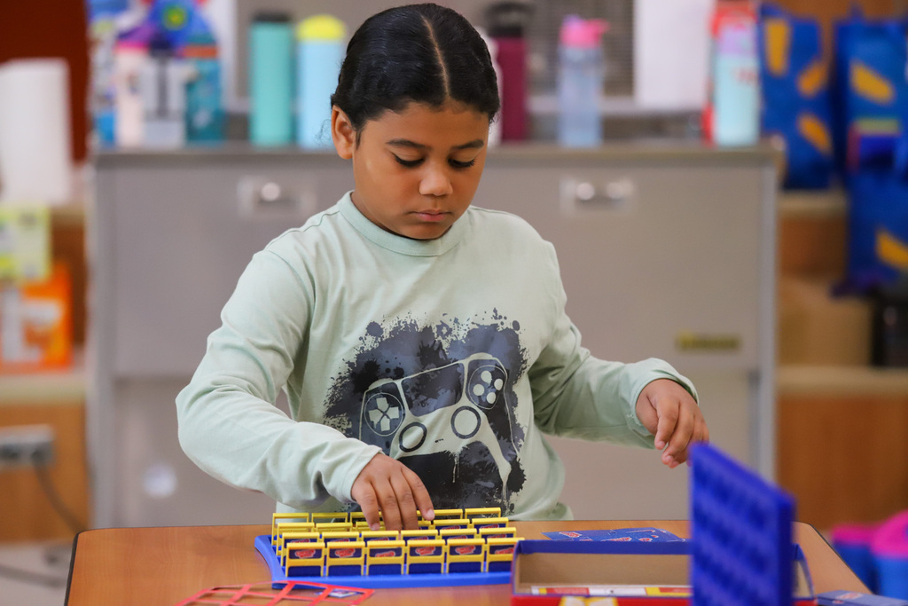 An elementary student sets up a board game in a classroom.
