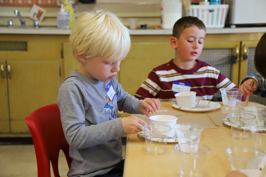 Elementary students use craft supplies to make slime in a classroom.