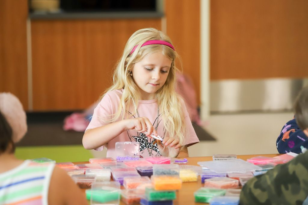 An elementary student threads a string with beads to make a bracelet at a school.