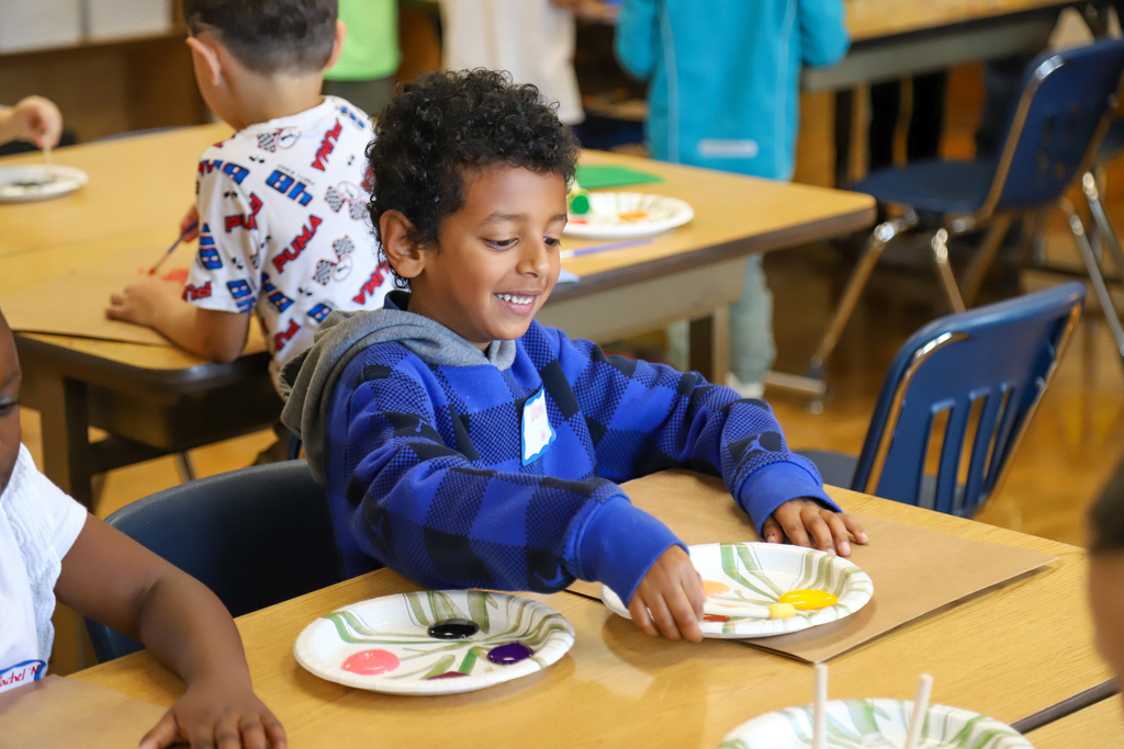 An elementary student smiles while using paint to decorate a paper bag monster.