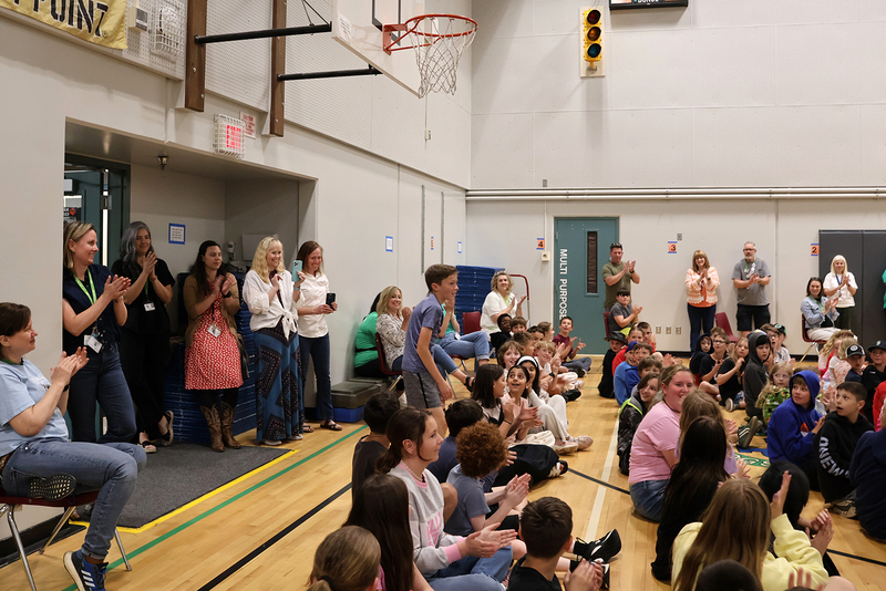 Elementary students and staff at an assembly clap for Owen Harwood as he stands to receive an award.