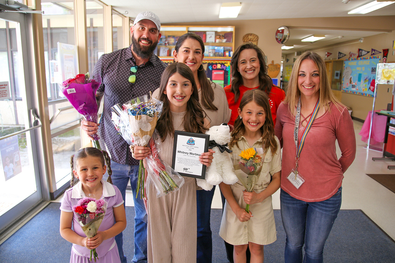 Whitney Wortman smiles with families and staff while holding flowers and an award.