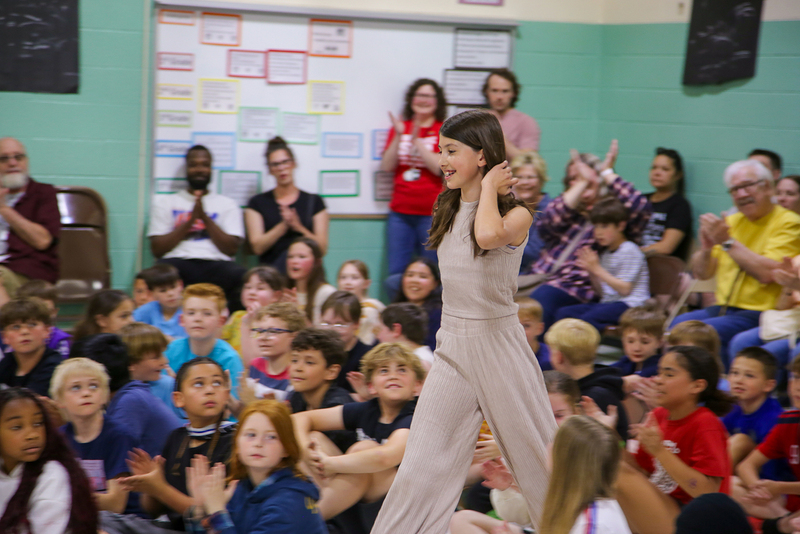 Elementary students and staff at an assembly clap for Whitney Wortman as she walks to receive an award.