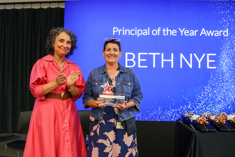 Beth Nye receives the Principal of the Year Award on stage, holding a glass trophy next to Board Director Nikki Otero Lockwood.