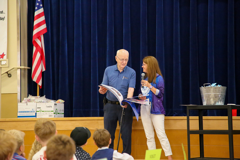 Lanny Burrill smiles with Anne Walter as they look through a scrapbook in front of an elementary school assembly.