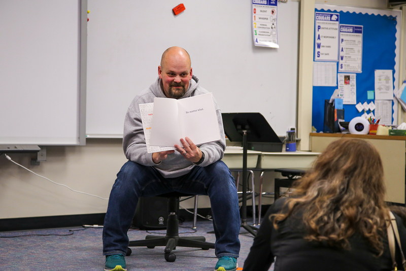 Principal Buz Hollingsworth holds open a book while reading to a group in a classroom.