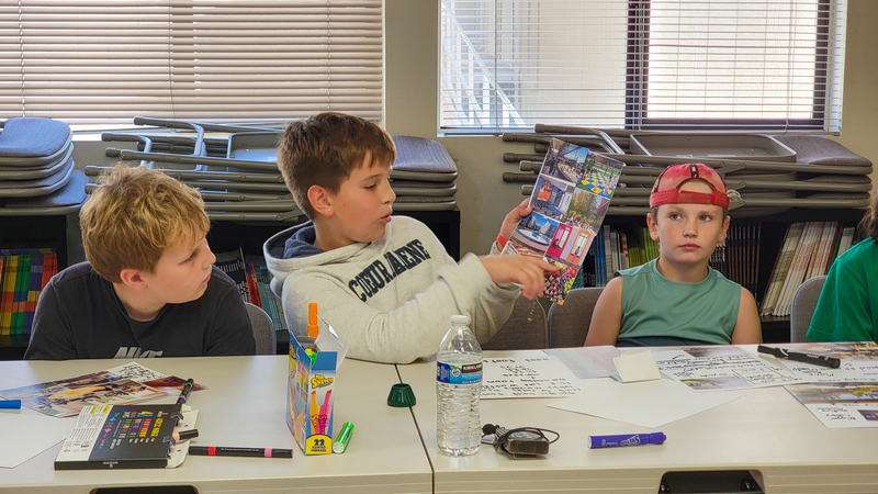 An elementary student holds up a collage of photos featuring different design ideas for a new elementary school.