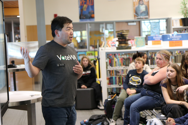 An election educator wearing a Vote WA tshirt speaks to students.