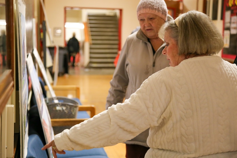 Woman in white sweater points to a rendering of Adams Elementary. Another woman looks on.