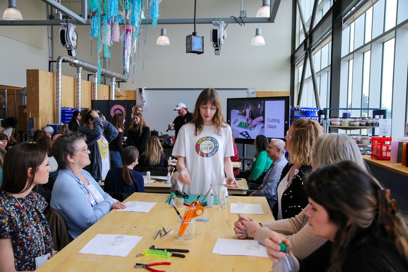 Female student instructs adults who are sitting at a table.