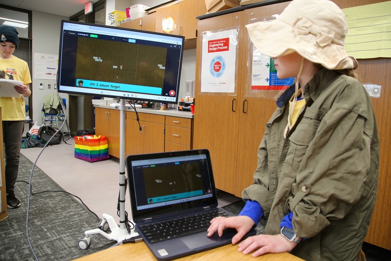 Girl with hat showcases video game on computer screen.