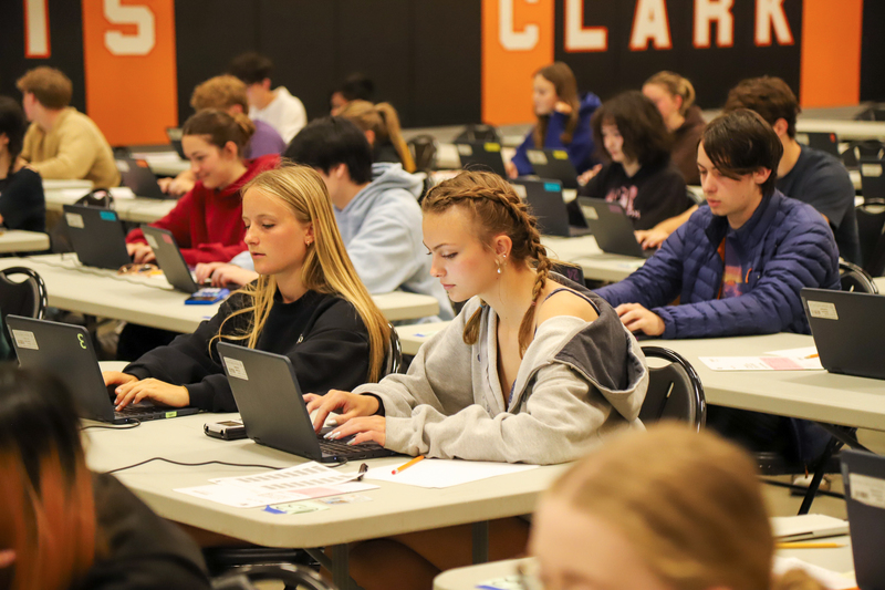 Two girls taking an exam on laptops amidst dozens of other students.