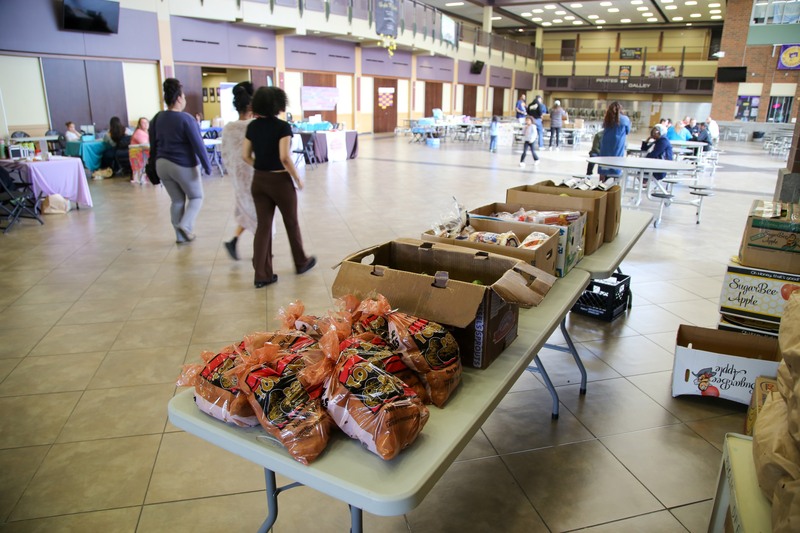 Bags of potatoes, boxes of bread, and fruits sit on a table at the entrance to the Rogers High School commons.