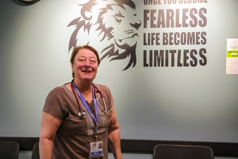 Woman standing in front of a wall painting of a lion next to the words, "When you become fearless, life becomes limitless." Marianne Fischer.
