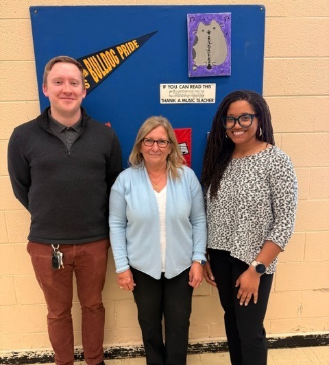 Three staff members are standing in front of a blue bulletin board , there are no words on the picture