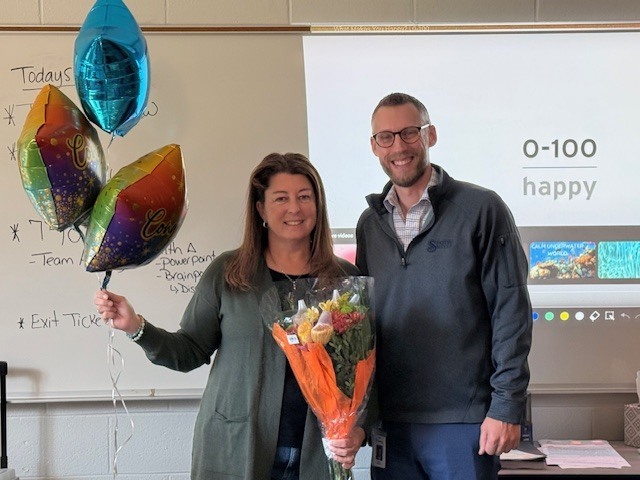 Mrs. Lavoy is standing next to Mr. Workman holding balloons and flowers