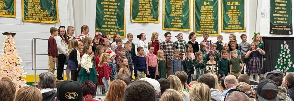 Students on a stage with Christmas trees singing holiday songs
