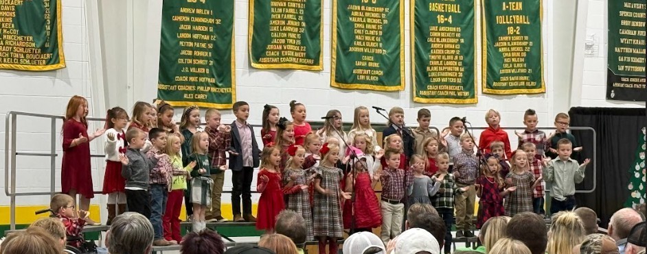 Students on a stage with Christmas trees singing holiday songs