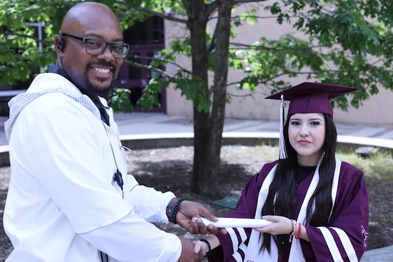 Paulina Arce in graduation attire receiving a diploma from her principal