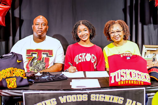 Genesis Harrell signing a letter of intent to Tuskegee University with her parents sitting next to her