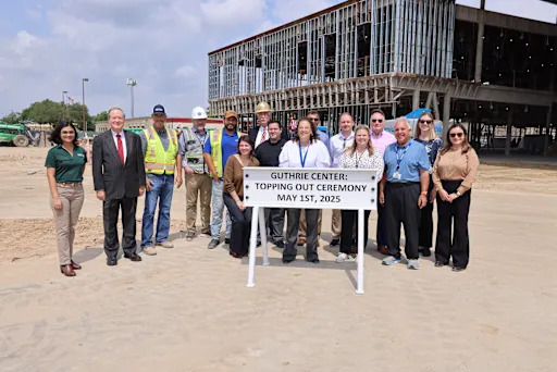 group of people showing off a sign reading "Guthrie Center: Topping Out Ceremony, May 1st, 2025"