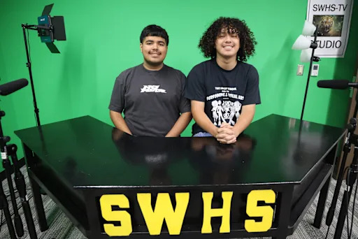 Tw ostudents behind spring woods high school news desk