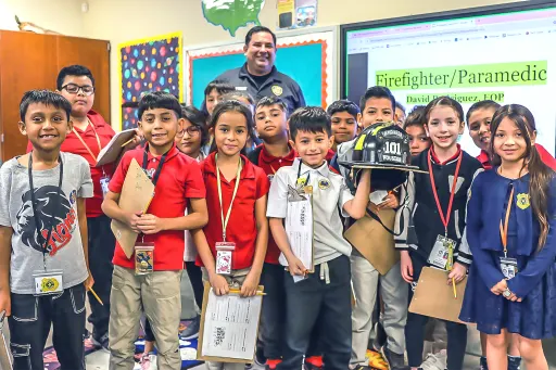 children stand grouped in front of a fireman. one of them holds the fireman's helmet