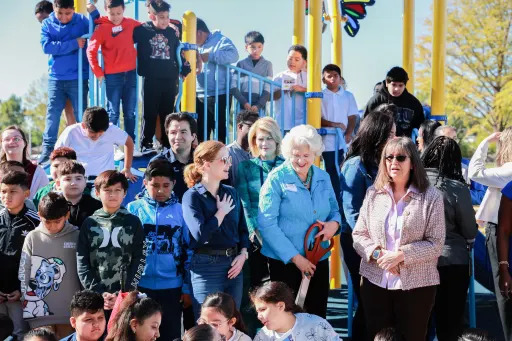 various kids and adults gathered around  playground steps, one of the mholding ceremonial ribbon-cutting scissors