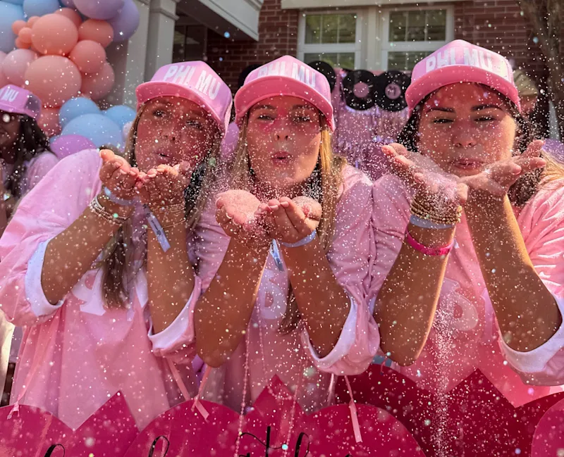 women in pink blowing glitter at the camera