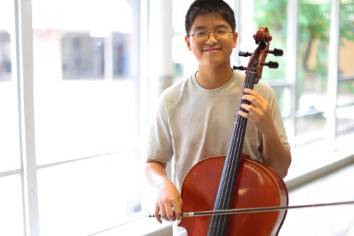 Sunny Seok smiling, holding a cello and bow
