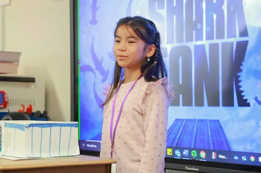 a student stands in front of a board reading "shark tank"