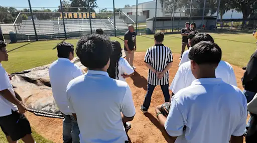 students gathered around a referee on a baseball field